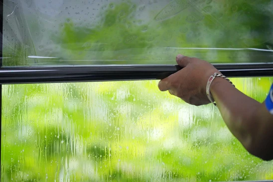 Un artisan professionnel en tenue de travail appliquant un film de protection transparent ou teint&eacute; sur une baie vitr&eacute;e ou une fen&ecirc;tre d'int&eacute;rieur, utilisant une raclette pour lisser le film et &eacute;liminer les bulles d'air, dans un environnement r&eacute;sidentiel moderne.